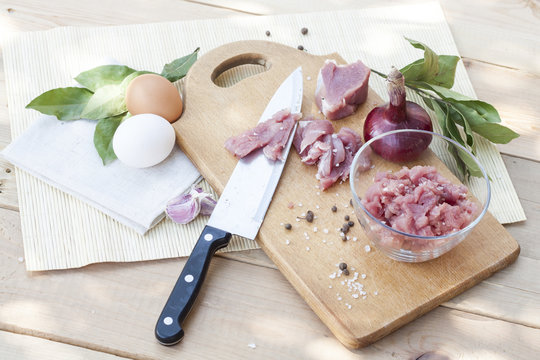 Raw chopped pork tenderloin with herbs in a glass bowl on a wooden board, selective focus