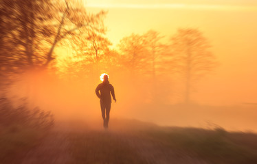 Runner on a gravel road during a foggy, spring sunrise in the countryside. With motion blur.