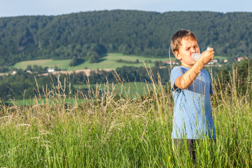 Boy using inhaler for asthma in village with summer sunset