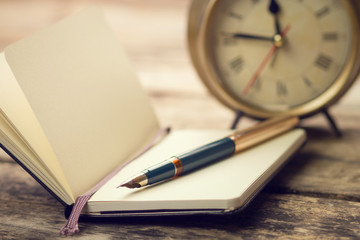 Open small notebook with fountain pen and old-fashioned alarm clock behind
