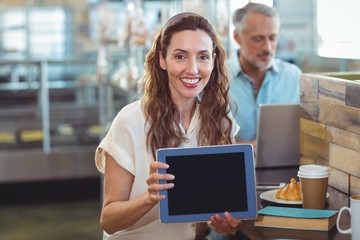 Pretty brunette looking at camera and showing tablet