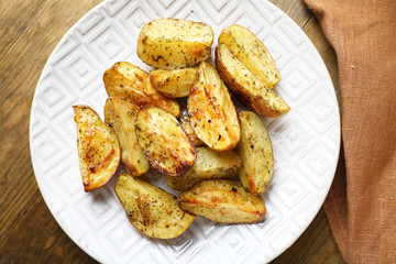 Baked spicy potatoes in white plate on wooden table, closeup