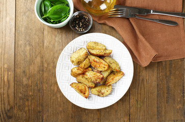 Baked spicy potatoes in white plate on wooden table, top view