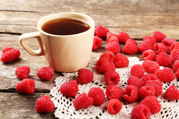 Fresh raspberries with cup of tea on wooden table with napkin, closeup