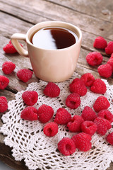 Fresh raspberries with cup of tea on wooden table with napkin, closeup