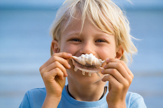 Beach fun, cute child holding shell over his mouth as a smile
