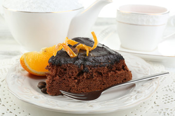 Piece of Chocolate cake and orange on plate, on table  background