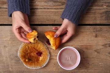 Female hands holding cup of coffee and cookies on wooden table close up