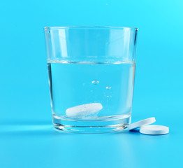 Glass of water and pills on blue background