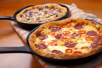 Two oven cooked cast iron skillet pan pizzas on wooden tabble