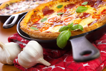 Cast iron skillet pan pizzas with garlic bulbs on wooden tabble closeup - 87888391
