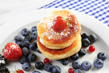 Fritters of cottage cheese with berries in plate on table, closeup