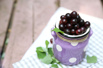 Red gooseberry in pail on wooden table close-up outdoors