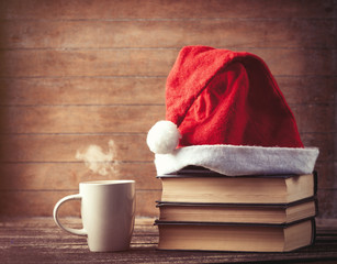 Obraz na płótnie Canvas Santas hat over books near hot cup of coffee or tea