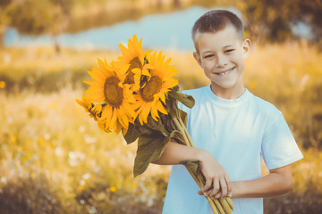 Happy boy with bouquet of sunflowers against summer field