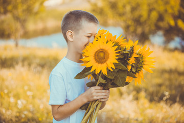 Happy boy with bouquet of sunflowers against summer field