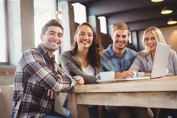 Smiling friends drinking coffee and using laptop