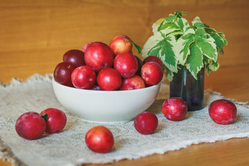 Plums in the white bowl on wooden table