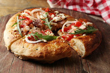 Greek homemade pizza with ham,onion, roasted tomato, creamy feta on wooden board, on table background