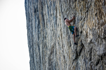 Young shirtless athletic man climbing on rock by water on ocean
