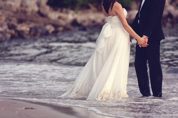 Fototapeta na wymiar Bride and groom holding hands at the beach