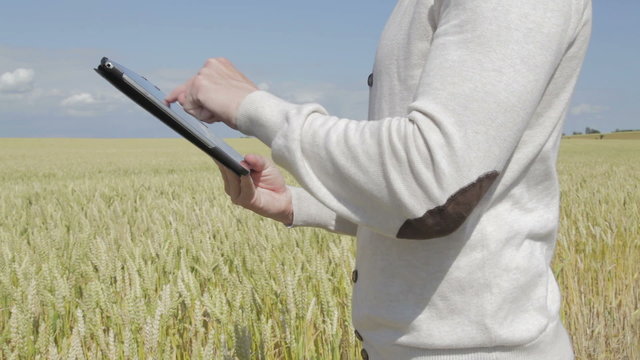 Caucasian man with a beige shirt standing at a field surfing on a tablet a summer day