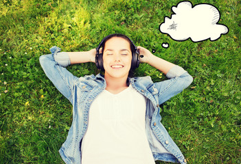 smiling young girl in headphones lying on grass