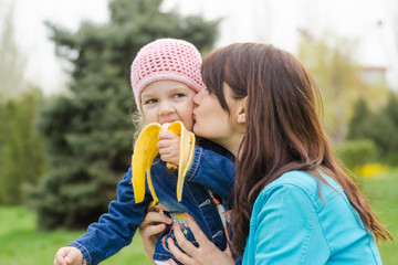 Mom kisses the girl who eats a banana on picnic