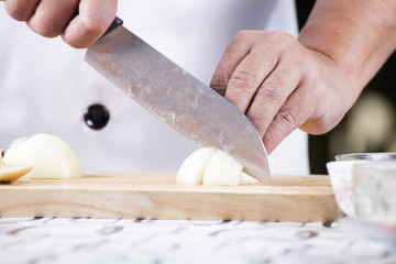 Chef cutting the onion on a wooden board