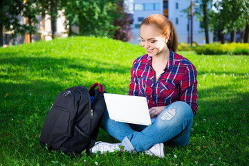 teenage student or school girl sitting with laptop in park