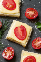 Hot sandwiches with cheese and tomato, greens, on a dark stone b
