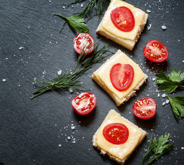 Hot sandwiches with cheese and tomato, greens, on a dark stone b