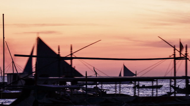 Sunset over Boracay beach fast motion, Philippines. Silhouettes of bangka boats and sailboats on the pink sky background