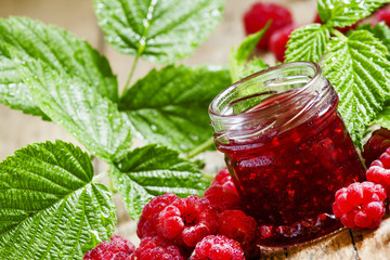 Raspberry jam with fresh raspberries and green leaves on the old