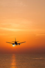 Fototapeta na wymiar Silhouetted commercial airplane flying above the sea at sunset