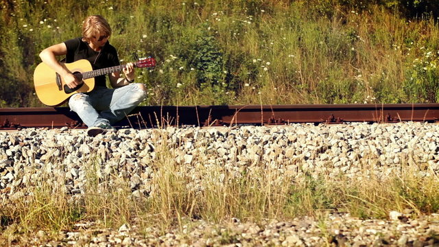 Young male guitarist playing sitting on the railway
