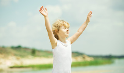 Happy child with raised arms standing near the sea. Vacation con