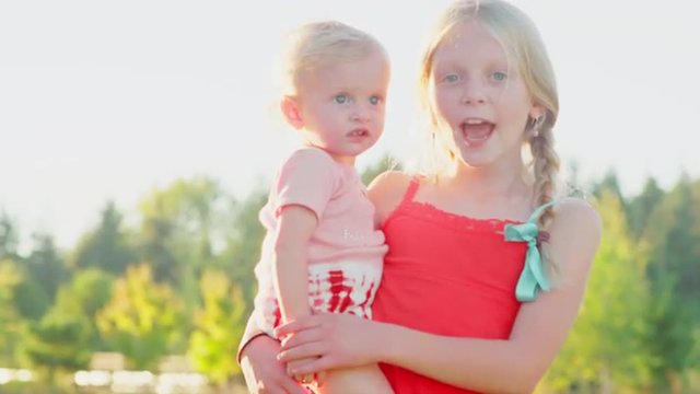 Young blonde girl holding her sister outside