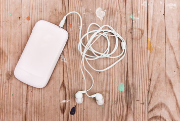 White smart phone with earphones  on grunge wooden desk.