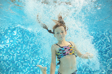 Girl jumps and swims in pool underwater, happy active child has fun in water, kid sport 