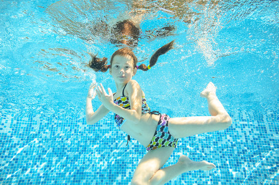 Girl jumps and swims in pool underwater, happy active child has fun in water, kid sport 