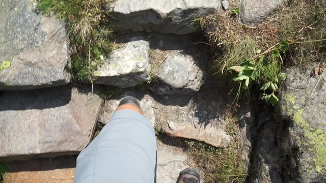 Hiker climbs up the rocky stairs of a mountain track. Hikers point of view.