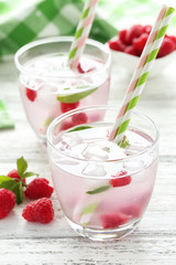 Raspberries and juice in glass on white wooden background