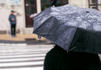 Woman with umbrella on rainy day waiting to cross the street