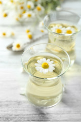 Glass of chamomile tea with chamomile flowers on color wooden background