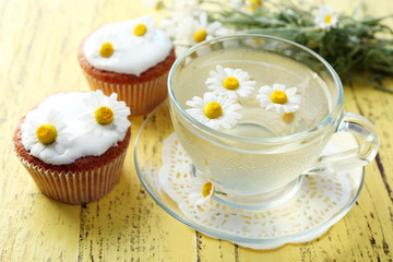 Cup of chamomile tea with chamomile flowers and tasty muffins on color wooden background