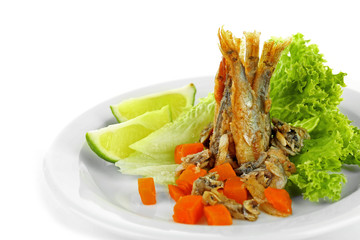 Fried small fish on plate with lettuce and lime isolated on white