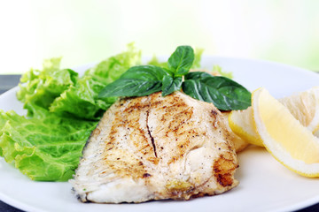 Dish of fish fillet with greens and lemon on bright background