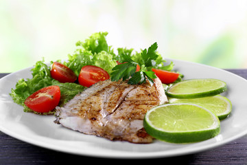 Dish of fish fillet with salad and lime on bright background