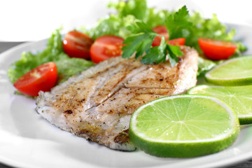 Dish of fish fillet with salad and lime on plate close up